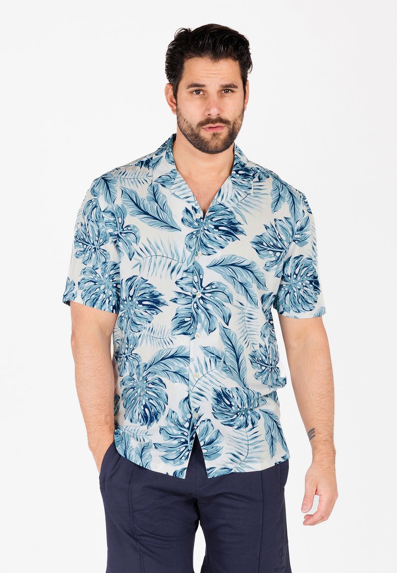 Chemise à manches courtes avec des boutons en tissu bleu clair, ornée d'un motif de feuilles tropicales dans différentes nuances de bleu. Col classique et coupe décontractée.