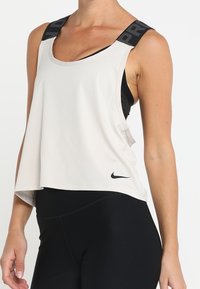 Camiseta sin mangas de color beige claro con tirantes anchos negros que presenta el texto "PRO". Está hecha de un material suave y lleva el logo de Nike en el dobladillo, con un corte relajado.