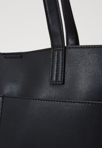 Zwarte totebag met een gestructureerde oppervlakte, voorzien van twee stevige handvatten en zichtbare stiksels langs de randen, wat een strakke uitstraling creëert.