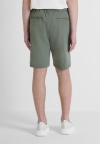 Shorts verts avec une ceinture élastique, deux poches arrière et une texture lisse. Associés à des baskets blanches, vus de l'arrière.