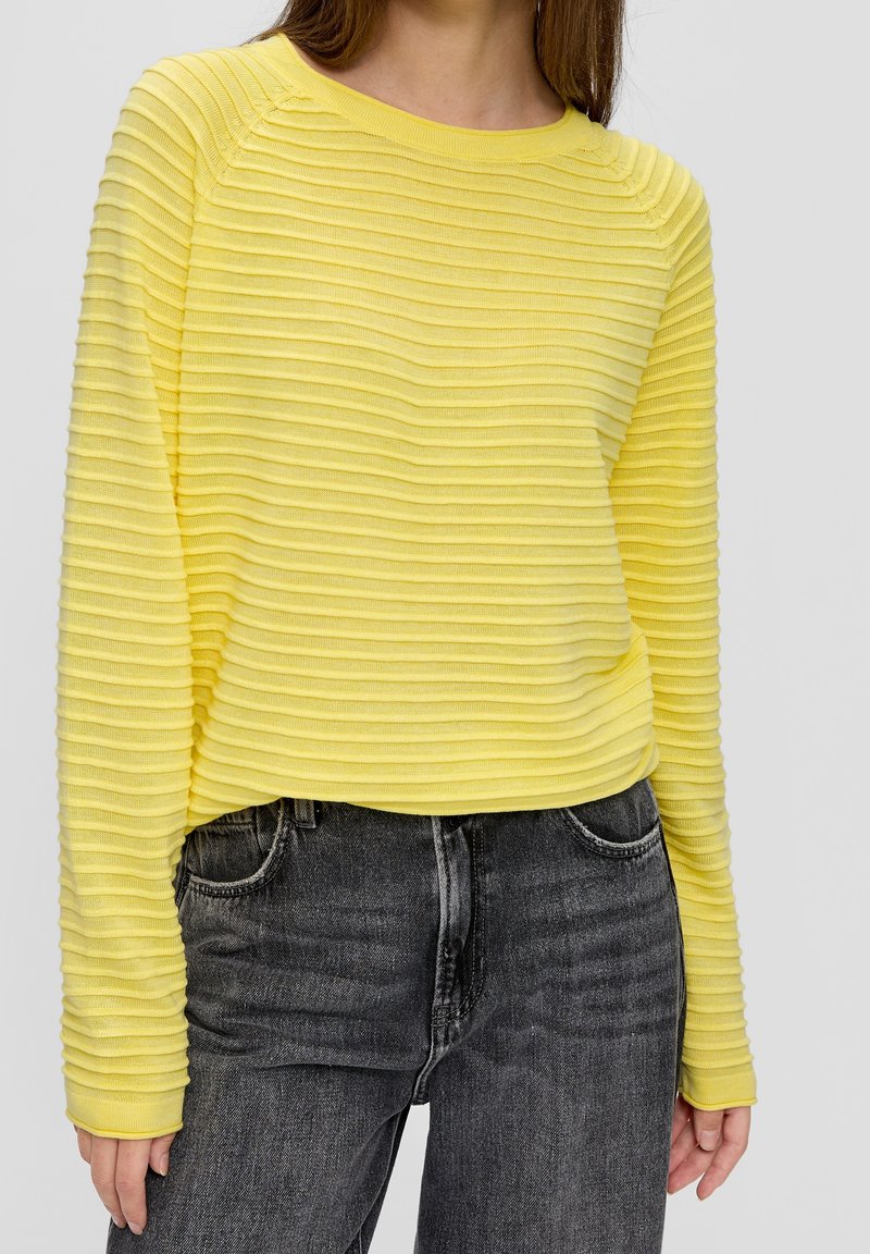 Gul ribbad långärmad tröja med rund halsringning, kombinerad med mörkgrå jeans som har en strukturerad yta och en avslappnad passform.