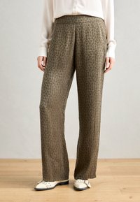 Groen gemustreerde wijde broek met een subtiele bladrimp, gemaakt van een soepele stof met een ontspannen pasvorm, gecombineerd met witte schoenen.