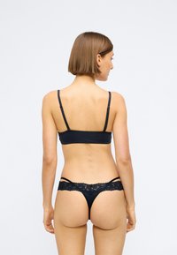 Schwarzes Wäsche-Set mit einem glatten, matten Bandeau-Top und einem Spitzen-Details-String mit offenen Seiten. Verstellbare Träger sind enthalten.