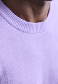 Ljuslila tröja med ribbad halsringning. Tyget verkar jämnt och mjukt, med en enkel och ren design. Inga mönster eller detaljer synliga.