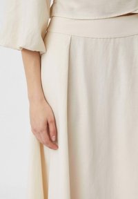 Beige, fließender Rock aus leichtem Stoff. Verfügt über einen flachen Bund und dezente Falten, die eine glatte Textur und neutrale Farbe zur Geltung bringen.