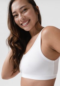 Weißer kabelloser Bralette aus glattem, elastischem Stoff, mit breiten Schulterträgern und tailliertem Schnitt. Keine sichtbaren Beschläge oder Verzierungen.