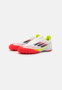 Scarpe da ginnastica bianche con suola rossa, strisce nere e accenti giallo neon. Materiale superiore liscio e suola testurizzata per una maggiore aderenza.