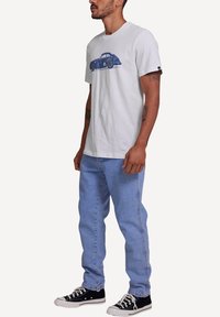 White cotton t-shirt featuring a blue car graphic; paired with light blue jeans and black sneakers with white soles. Casual fit.