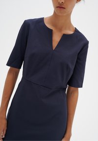 Marinblå kortärmad klänning med V-ringning, har en figurnära överdel och en slät yta. Minimalistisk design med rena linjer.