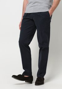 Pantaloni in cotone blu navy con vestibilità dritta, dotati di tasche laterali e una texture sottile. Abbinati a scarpe in suede marrone scuro.