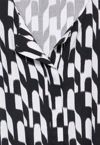 Svart- och vitmönstrad blus med krage, där abstrakta former och linjer skapar en texturerad visuell effekt.