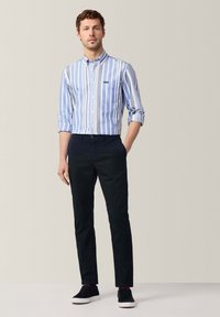 Gestreiftes blaues und weißes Hemd mit Knopfverschluss und einer Brusttasche, kombiniert mit schwarzen Hosen und dunklen Sneakern. Weicher Stoff, taillierte Passform.
