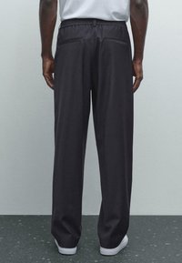 Zwarte wijde broek met een gedeeltelijk elastische tailleband, twee achterzakken en een gladde textuur, gecombineerd met witte sneakers.
