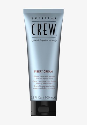 Jonge man met kort, gestructureerd haar, gekleed in een donker gewatteerd vest en hoodie, naast tekst die de voordelen van vezelcrème in het Frans beschrijft.