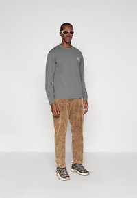 Szary longsleeve, beżowe spodnie z korduroyu i masywne sneakersy w odcieniach szarości i kremu. Okrągłe okulary przeciwsłoneczne dopełniają outfit.