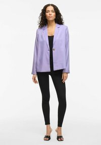 Lavendel blazer met een enkele gouden knoop, gladde stof, getailleerde pasvorm. Gecombineerd met een zwarte top en legging, zwarte open tenen schoenen.