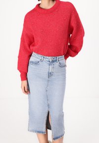 Röd stickad tröja med en texturerad finish och sänka axlar, i kombination med en ljusblå denimpennkjol med en framfick.