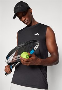 Camiseta atlética sin mangas negra con un logo blanco; gorra negra con "BORG" en relieve; el jugador sostiene una raqueta de tenis y una bola verde brillante.