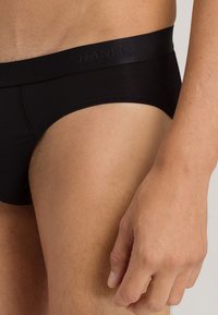 Zwarte herenboxershort van een gladde stof, met een zachte tailleband met reliëfbranding en een strakke pasvorm rond de dijen.