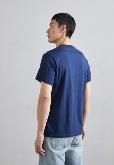 T-shirt in cotone blu navy con colletto a giro, maniche corte e orlo dritto, abbinata a jeans in denim chiaro con tasche posteriori.