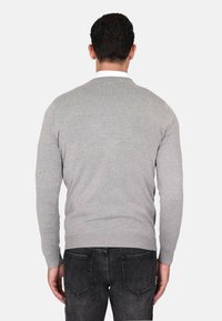 Maglione grigio lavorato a maglia con scollo rotondo, maniche lunghe e orlo a coste. Indossato sopra jeans scuri. Tessuto liscio, design semplice senza fantasie.