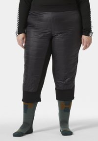 Zwarte, gewatteerde cropped broeken met een elastische tailleband, gedragen met gestreepte teal sokken met geometrische accenten en contrasterende kleuren.