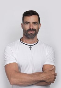 T-shirt bianca a maniche corte con una collana intrecciata nera caratterizzata da un pendente a croce in argento, su uno sfondo chiaro e semplice.