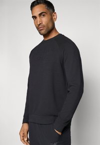 Juodas megztinis su apvalia iškirpte, ilgomis rankovėmis ir tekstūruotu logotipu priekyje. Pagamintas iš minkštos medžiagos, laisvo silueto.