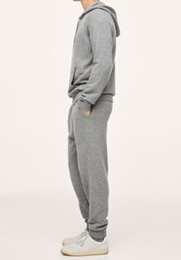 Grijze hoodie met een buidelzak, gecombineerd met bijpassende sweatpants. Beide hebben een zachte textuur, aansluitende cuffs en een ontspannen pasvorm.