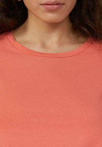 Koszulka typu crew neck z koralowego koloru, wykonana z miękkiej bawełny, z gładką fakturą i krótkimi rękawami. Minimalistyczny design bez widocznych wzorów.