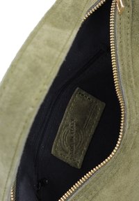 Interno della borsa in suede verde oliva con fodera in tessuto nero. Presenta una cerniera dorata e un'etichetta "Made in Italy" su una toppa testurizzata.