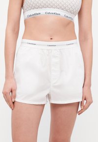 Fehér pamut rövidnadrág elasztikus Calvin Klein derékkal, sima textúrával és laza szabással. Minimalista dizájn, térdhosszú.