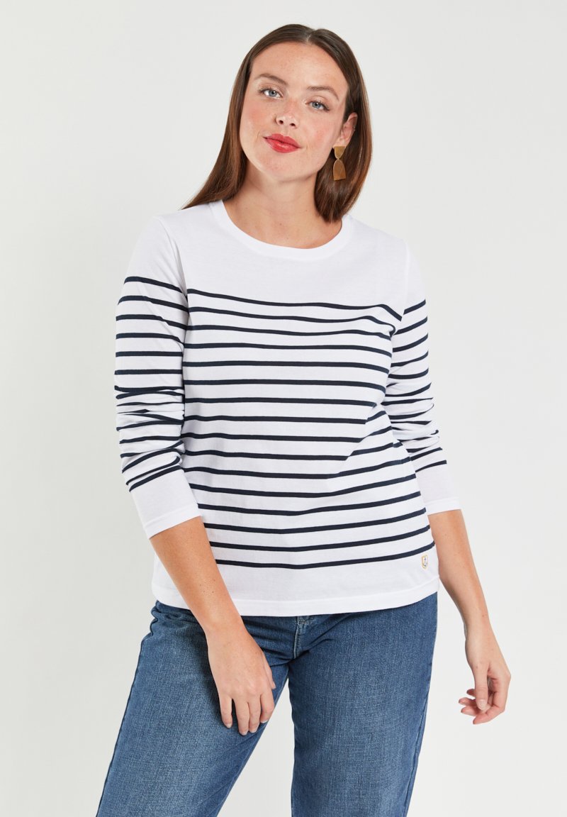 Hvid langærmet skjorte med marineblå vandrette striber, rund halsudskæring og subtilt brandlogo på kanten. Parret med blå jeans.