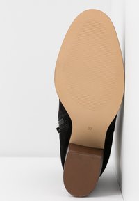 Zapato de ante negro con suela de goma, que presenta un tacón marrón texturizado y una marca de tamaño "37" en la parte inferior. Acabado suave.