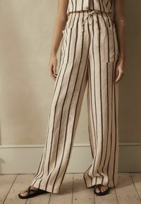 Pantalons en lin légers avec une coupe décontractée, présentant des rayures verticales noires, des poches latérales et une taille élastique avec un cordon de serrage.