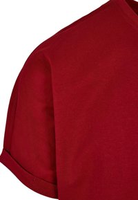 Tricou roșu din bumbac, cu decolteu în formă de cerc, mâneci scurte și o suprafață ușor texturată. Prezintă o croială lejeră și tivul mânecilor pliat.