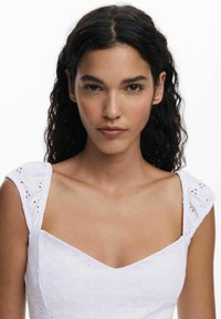 Valge kleit ruudukujulise dekoltee, broderitud lillemotiivide ja lühikeste puhvärvlitega, millel on silmadega detailid. Sile kangas.