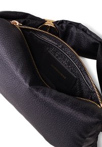 Sac à main noir texturé avec une fermeture éclair dorée, présentant un intérieur à motifs et une étiquette en cuir noir à l'intérieur. Design lisse et structuré.
