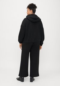 Svart hettegenser med senkede skuldre, elastiske mansjetter og matchende vide bukser. Glatt tekstur, minimalistisk design, ingen mønstre.