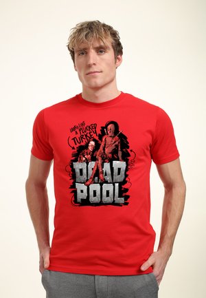 Man wearing a red Deadpool t-shirt featuring Deadpool sitting with swords and the text "Looks like a plucked turkey."