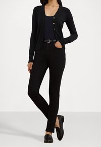 Svart cardigan med V-ringning och knappar, kombinerad med svarta skinny jeans och svarta loafers. Slät textur och åtsittande design genom hela plagget.