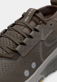 Chaussure de trail Nike vert olive foncé avec tissu perforé, points réfléchissants, lacets durables et texte "ALL NIGHT" sur la boucle de la languette.