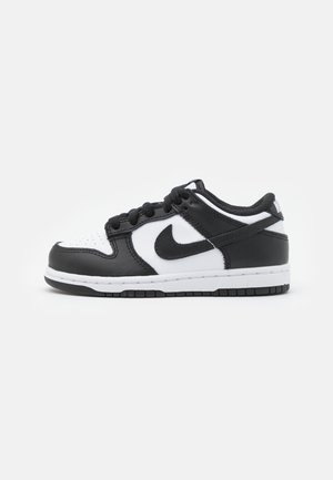 Baskets basses Nike noires et blanches avec lacets, bout perforé et logo swoosh noir sur le panneau latéral blanc.