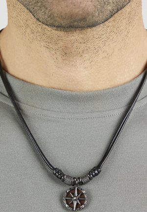 Schwarze Lederkordel-Halskette mit einem braunen hölzernen Kompassanhänger, der ein Metallstern-Design und filigrane silberne Akzente aufweist.