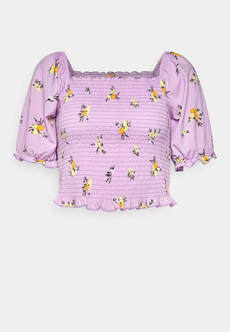 Top floral lila con mangas abullonadas, textura fruncida y dobladillo con volantes. Presenta patrones de flores amarillas y negras sobre una tela suave.