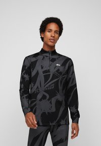 Schwarzes, langärmliges Sportoberteil mit hohem Kragen, Reißverschluss vorne und auffälligen grauen Grafikmustern. Hergestellt aus dehnbarem Stoff für einen hohen Tragekomfort.