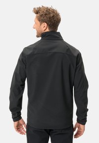 Čierna softshellová bunda s vysokým golierom, ľahkým materiálom a hladkou textúrou. Má minimalistický dizajn a priliehavý strih.