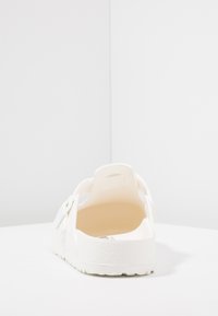 Zapato blanco sin cordones con diseño recortado, textura suave, forma redondeada y suela duradera. El interior tiene un acabado suave para mayor comodidad.