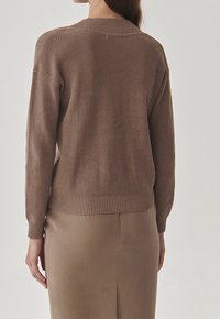 Bruine geribbelde gebreide trui met een relaxte pasvorm, kenmerken een ronde halslijn en doorgezakte schouders, gecombineerd met een bijpassende rok.