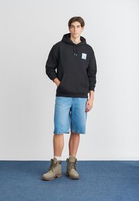 Črna kapuca s sprednjim žepom, turkizne vrvi in grafičnim detajlom. Ujemite jo s svetlo modrimi jeans kratkimi hlačami in rjavimi škornji.